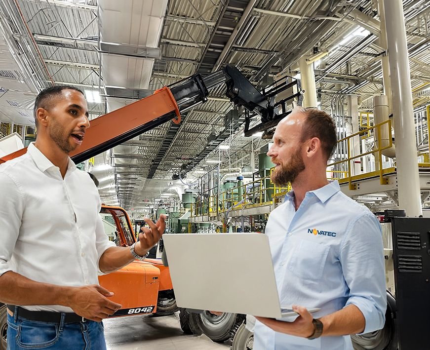 Two Novatec systems engineers reviewing a layout on a laptop on a plant floor